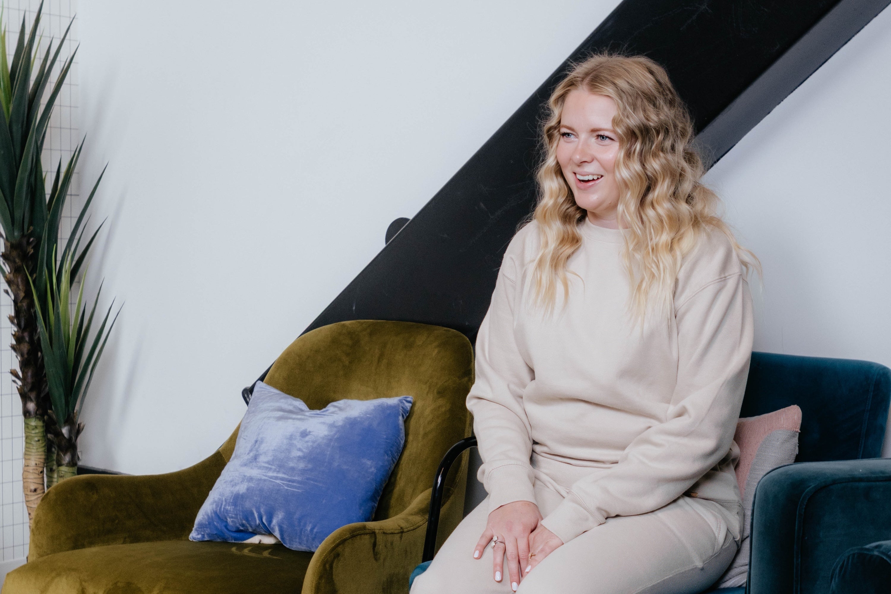 Woman sitting on a blue chair in a modern interior setting with green and yellow chairs.