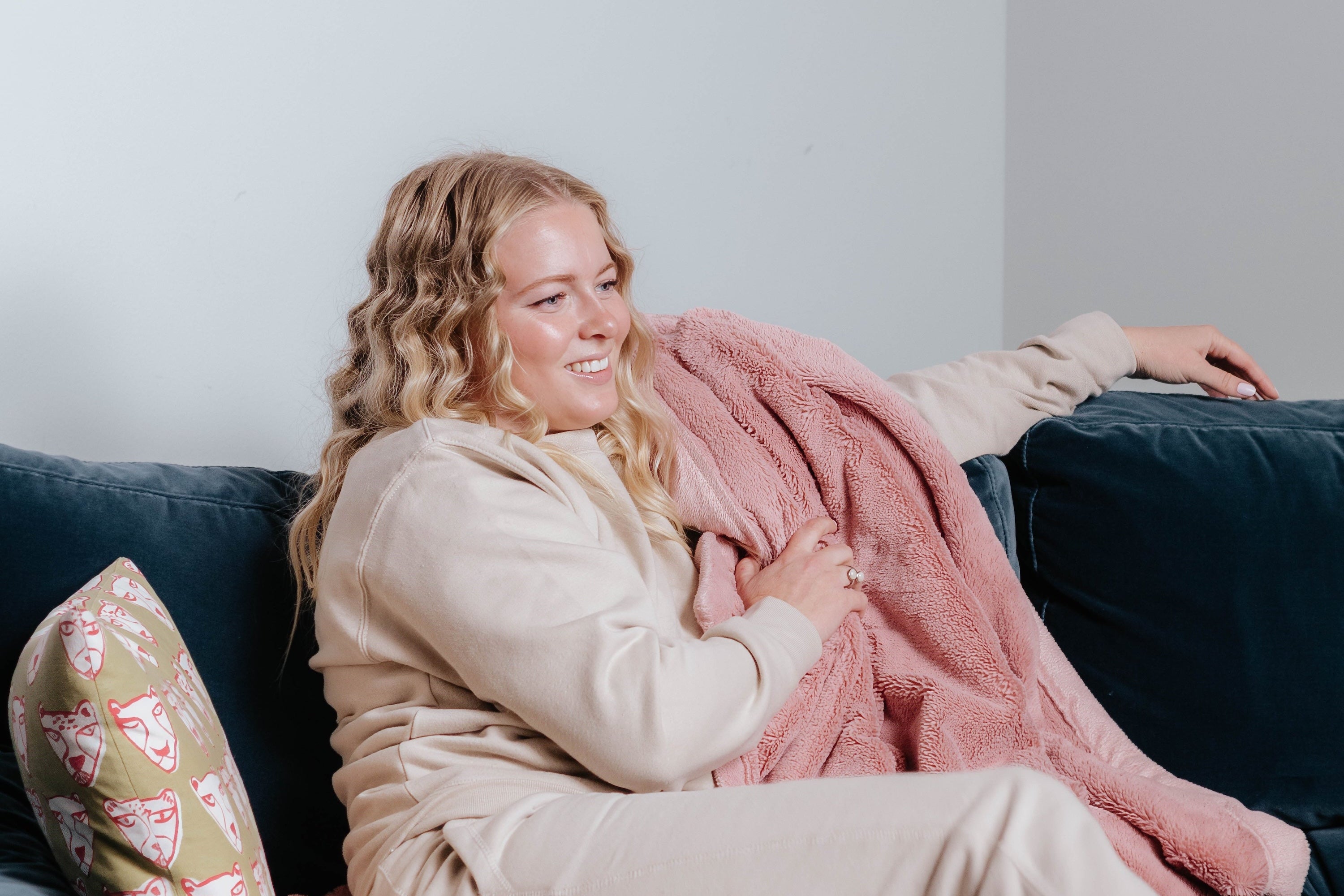 Woman sitting on a couch with a pink blanket and floral pillow